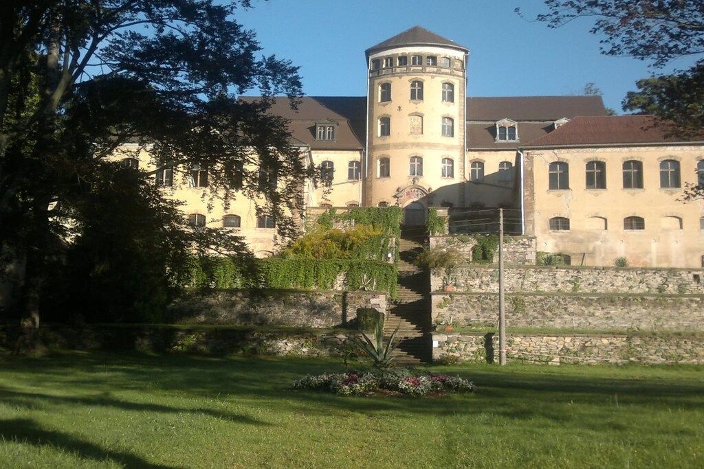 A historic building with a tower, surrounded by a well-maintained garden and a stone wall.