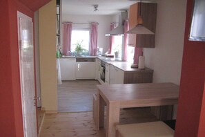 Eine kompakte Küche mit Essbereich, Holzboden und Blick ins Freie durch das Fenster.