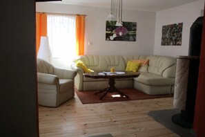 Ein Wohnzimmer mit einem beigefarbenen Sofa, einem runden Tisch mit Kerze und einer Lampe.