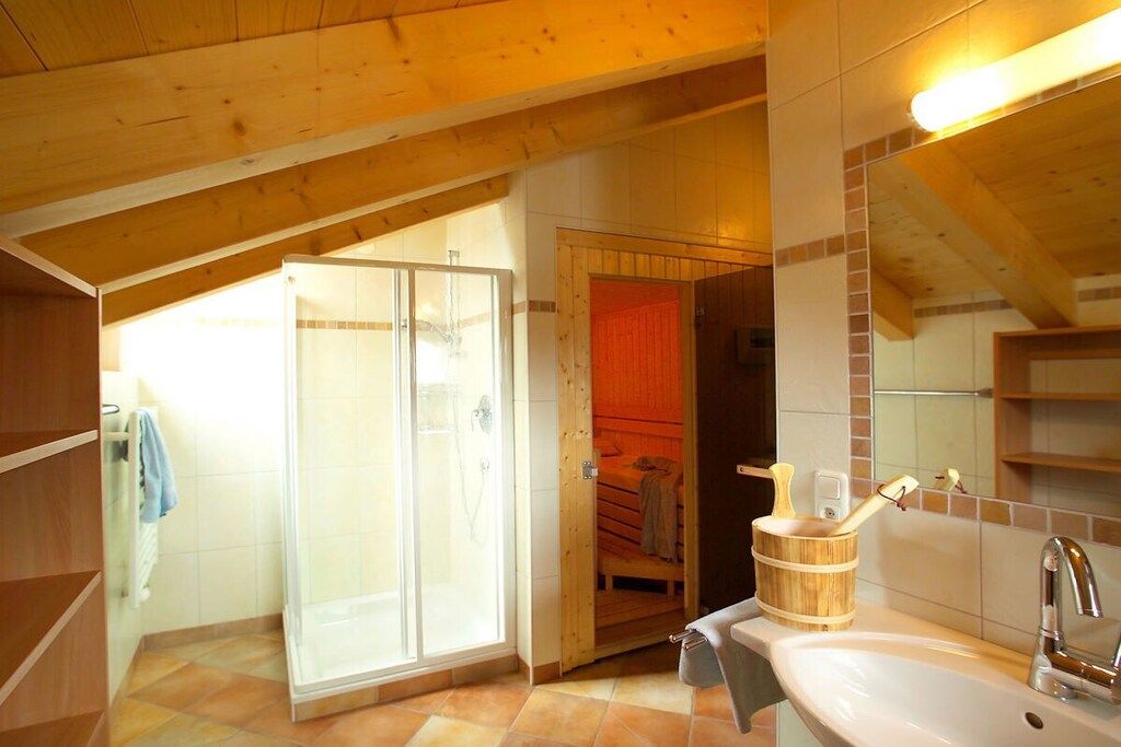 A bathroom with a shower, a wooden door, a sink, and a mirror.