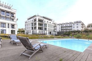 Ein Swimmingpool mit Liegestühlen und einer Holzterrasse, umgeben von modernen Gebäuden.
