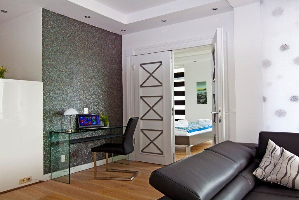 A modern bedroom with a glass desk, a black leather sofa, and a bed with striped bedding.