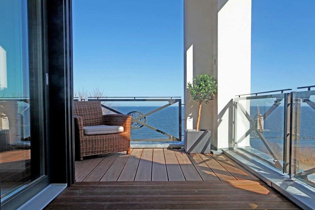 A balcony with a wicker chair and a small plant, overlooking a body of water.