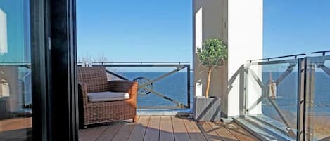 A balcony with a wicker chair and a small plant, overlooking a body of water.