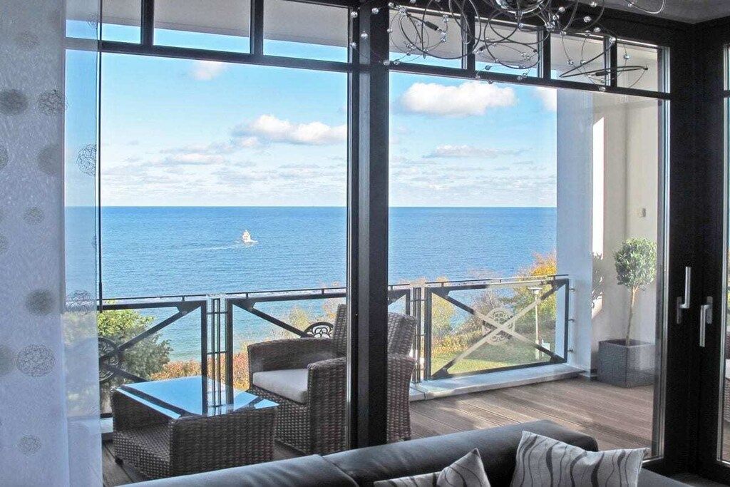 A balcony with a view of the sea, wicker furniture, and a glass door.