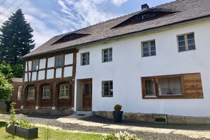 Ein zweistöckiges Haus mit weißer Fassade und dunklem Dach.