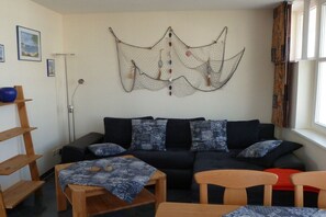 Ein Wohnzimmer mit einem schwarzen Sofa, Holzstühlen, einem Couchtisch mit gemustertem Tischläufer und einem Wandbild.