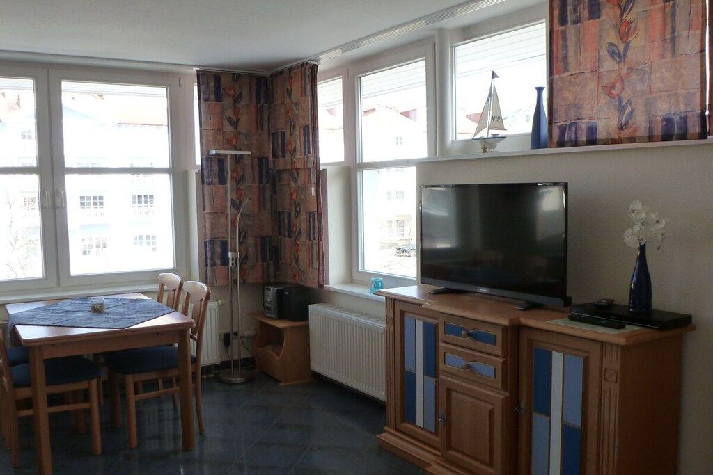 A room with a dining table, chairs, a television, and a radiator.