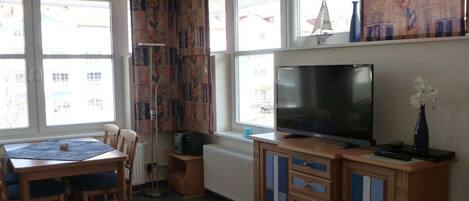 A room with a dining table, chairs, a television, and a radiator.