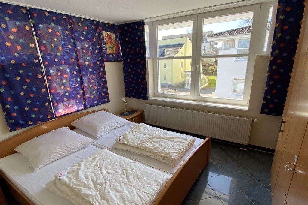 Una camera da letto con due letti, una finestra con tende, un termosifone e vista su case.