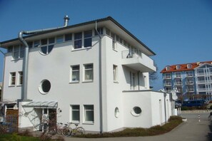 A white multi-story building with balconies, a bicycle parked in front, and a clear sky. - Holiday apartment with 1 bedroom (Zinnowitz)