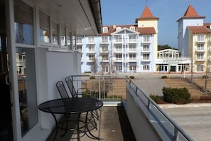A balcony with a table and chairs, overlooking a building with multiple windows and a red roof. - Holiday apartment with 1 bedroom (Zinnowitz)