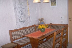 Ein Essbereich mit Holztisch und -stühlen, einer Vase mit Blumen und einem Wandvorhang mit Blumenmuster.