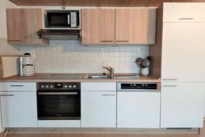 A modern kitchen with a microwave, oven, dishwasher, and wooden cabinets. - Holiday apartment with 2 bedrooms (Kleingießhübel)