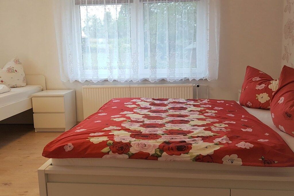 Une chambre à coucher avec un lit, une table de chevet, une fenêtre avec des rideaux et un radiateur.