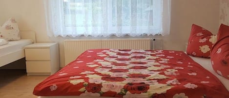 A bedroom with a bed, a nightstand, a window with curtains, and a radiator.