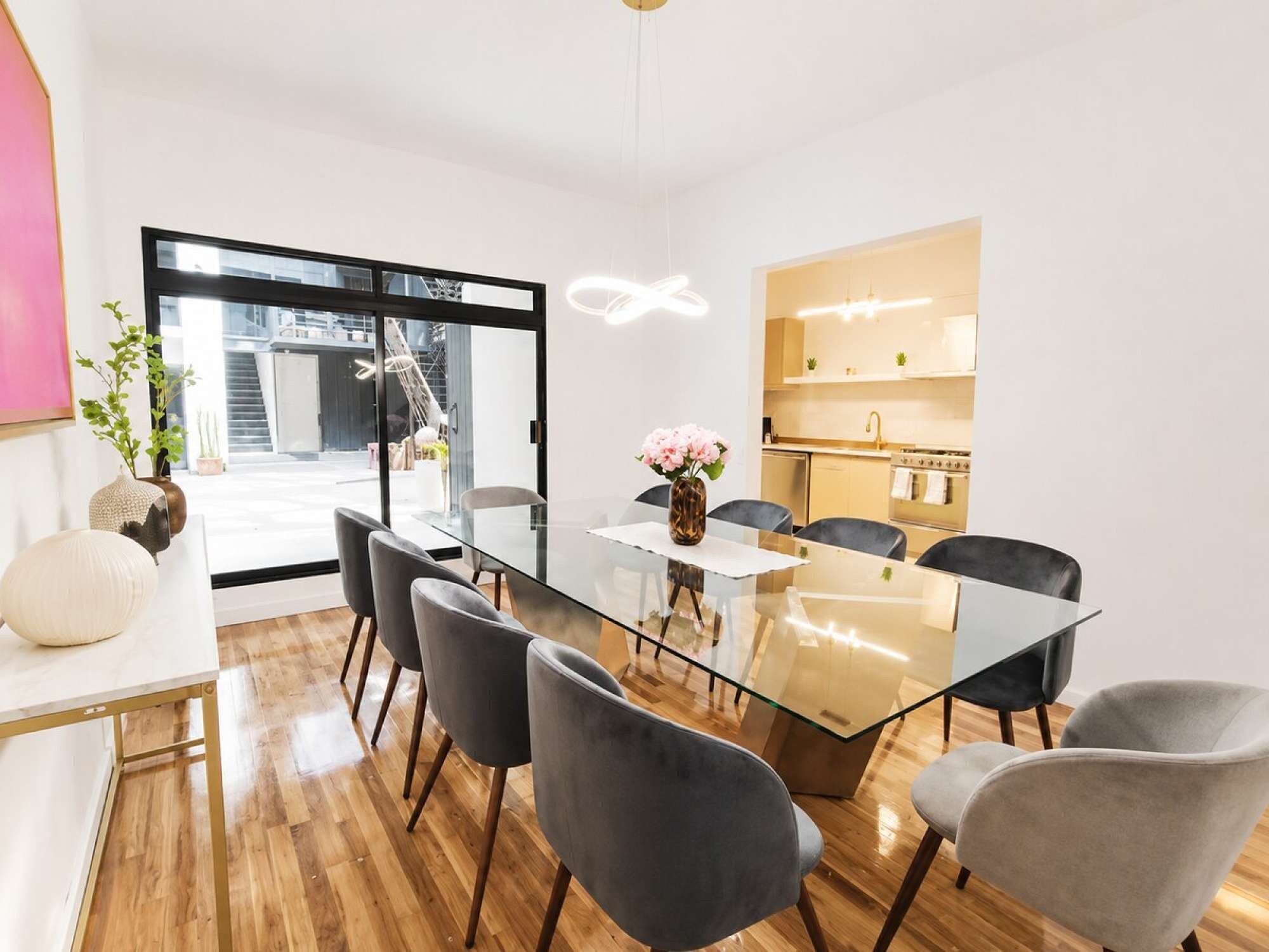A modern dining area with a glass table, grey chairs, and a view of the outside.