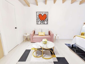 Quarto moderno e minimalista com sofá, duas mesinhas de apoio, uma mesa de centro e uma obra de arte decorativa em formato de coração na parede.