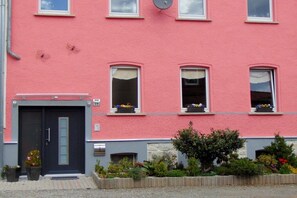 A pink building with a dark door, windows with flower boxes, and a small garden area. - Bauer 2 Mountain View (Thale)