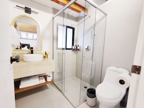 A modern bathroom with a glass shower enclosure, a white toilet, and a vanity with a mirror. - Laila Casa + Luz María 5 · Polanco, sleeps 15 · 5.5 baths (Ciudad de México)