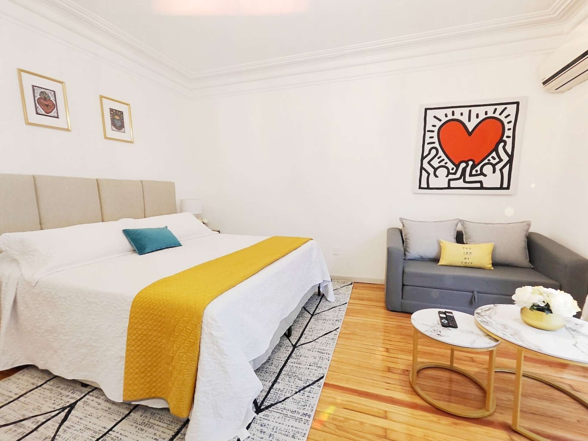 Ein modernes Schlafzimmer mit einem Bett, einer Couch, einem Couchtisch und Kunstwerken an den Wänden.