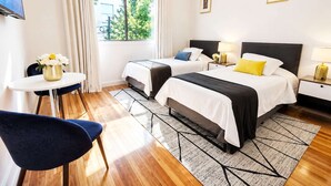 Una habitación de hotel con dos camas, un escritorio, una silla y un ventanal con cortinas.