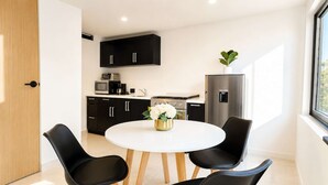 Una cocina moderna con armarios negros, una mesa de comedor blanca y cuatro sillas, y un refrigerador.