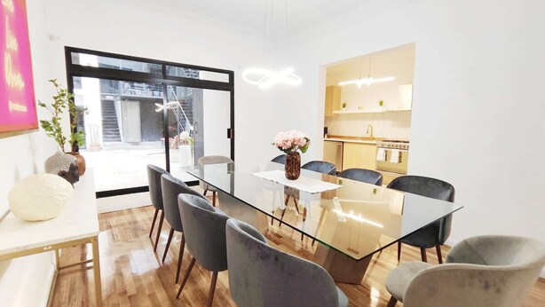 Un comedor moderno con una mesa de vidrio, sillas grises y vistas al exterior.