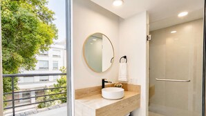Un baño moderno con cabina de ducha de vidrio, un espejo redondo y un lavabo con encimera color beige.