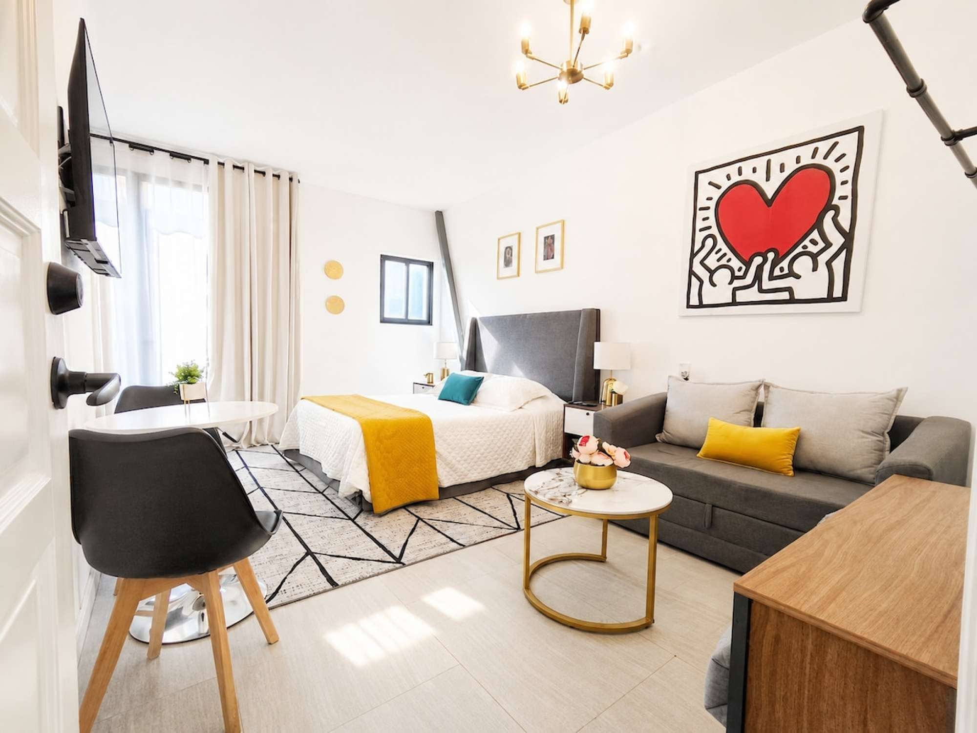 A modern hotel room with a bed, sofa, and a dining area.