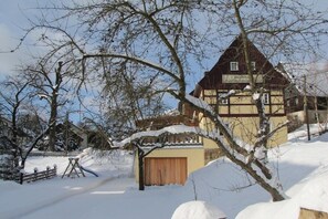 Ein traditionelles Holzhaus mit geneigtem Dach, umgeben von verschneitem Gelände und kahlen Bäumen.