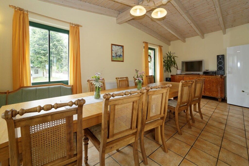 A dining area with a wooden table and chairs, a television, and a refrigerator.