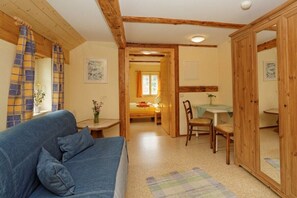 Ein gemütliches Zimmer mit einem blauen Sofa, Holzbalken, einer kleinen Essecke und einem Spiegelkorpus.