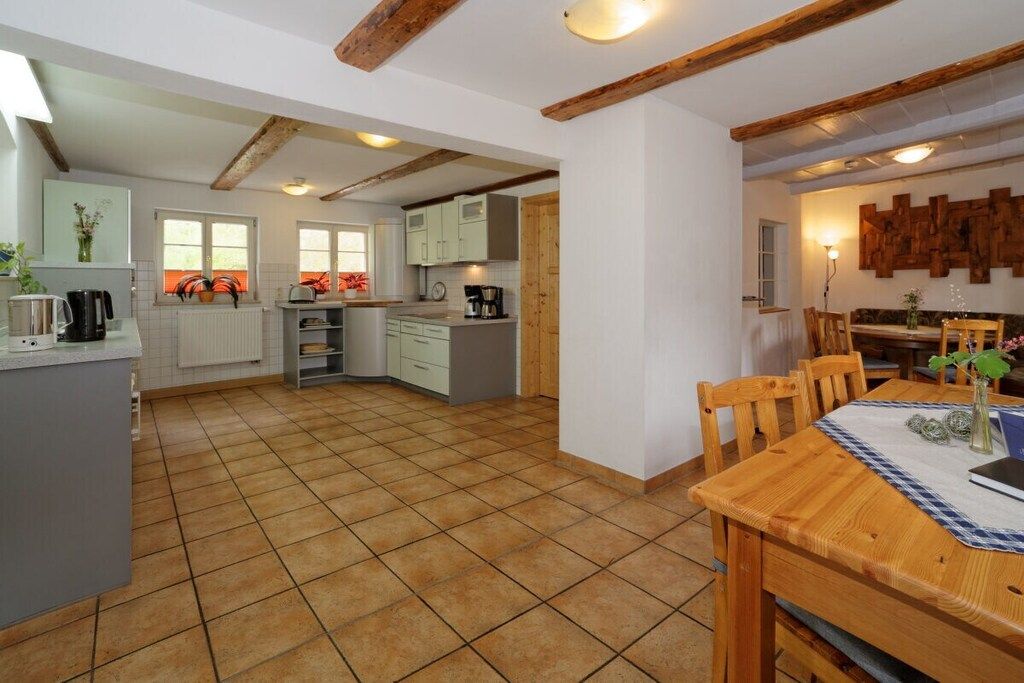 Een ruime keuken met een eethoek, met een houten tafel en stoelen, een betegelde vloer en een wit plafond met zichtbare balken.