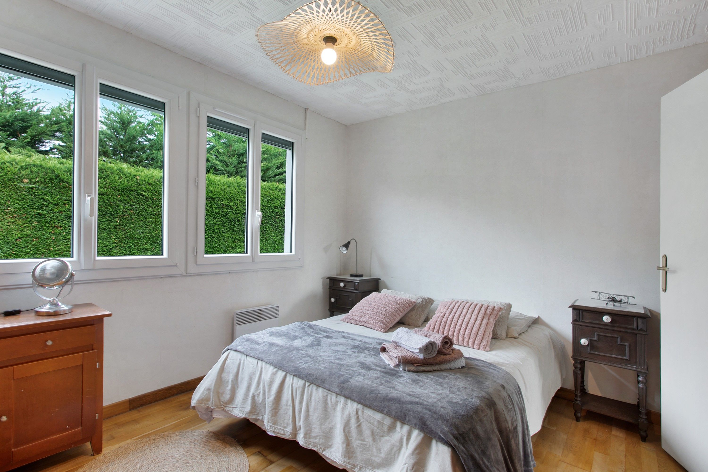 Un dormitorio con cama, mesitas de noche, cómoda y ventana con vistas a vegetación.