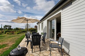 An outdoor patio with a grill, chairs, and an umbrella. - Holiday home 'Petite Maison de Kervenou' with private terrace, garden and Wi-Fi (Goudelin)