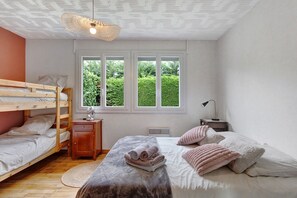 Un dormitorio con literas, una mesita de noche, un calentador, una ventana con vistas a zonas verdes y una lámpara colgante.