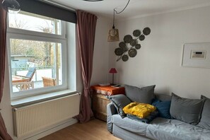 Ein Wohnzimmer mit grauem Sofa, einem Fenster mit Vorhängen, einer Heizung und einem an der Wand befestigten dekorativen Blattkunstwerk.