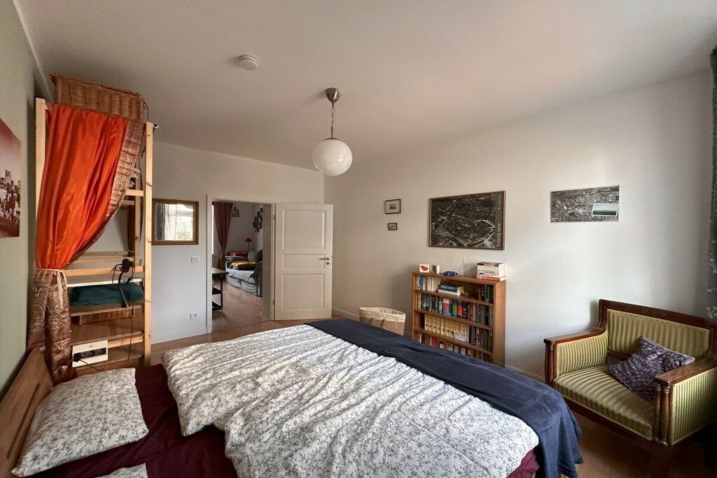 A bedroom with a bunk bed, a single bed, a bookshelf, a chair, and a door leading to another room.