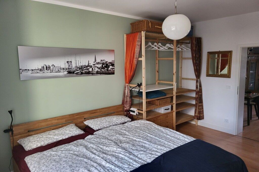 Une chambre à coucher avec un lit en bois, un tableau représentant un paysage urbain, une armoire et un luminaire suspendu.
