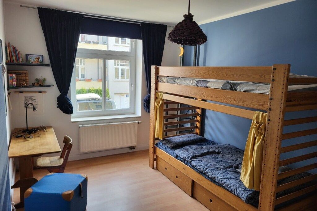 Een stapelbed met een bureau en stoel, een raam met gordijnen en een hanglamp.