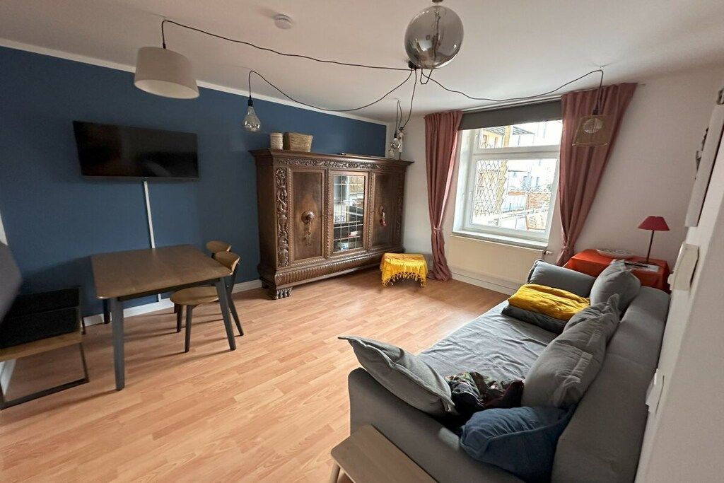 Ein Wohnzimmer mit einer Couch, einem Holzschrank, einem Fernseher und einem Fenster mit Vorhängen.