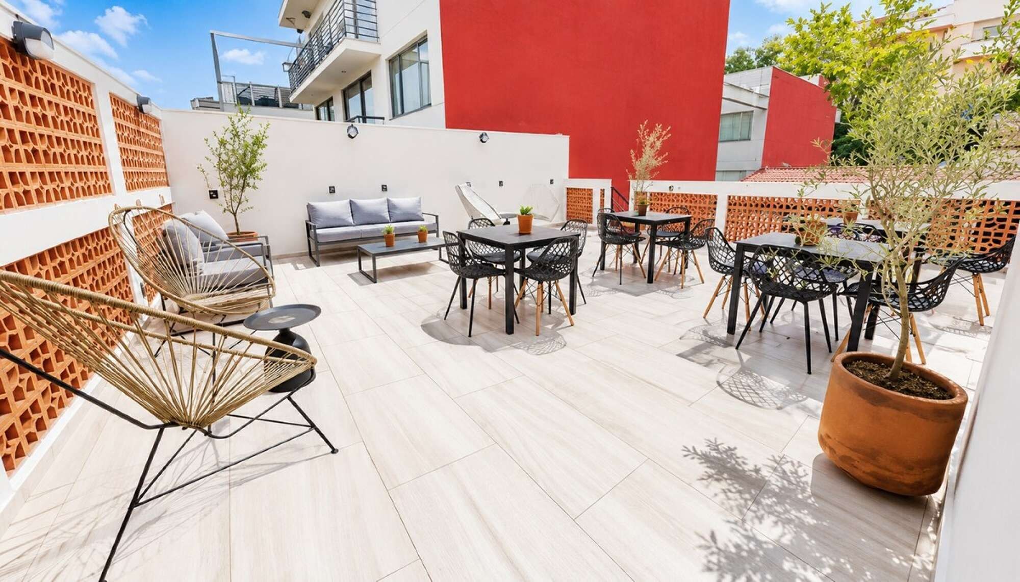 Un espace extérieur aménagé en terrasse, avec des coins salon comprenant des chaises et un canapé, ainsi qu’une table à manger.