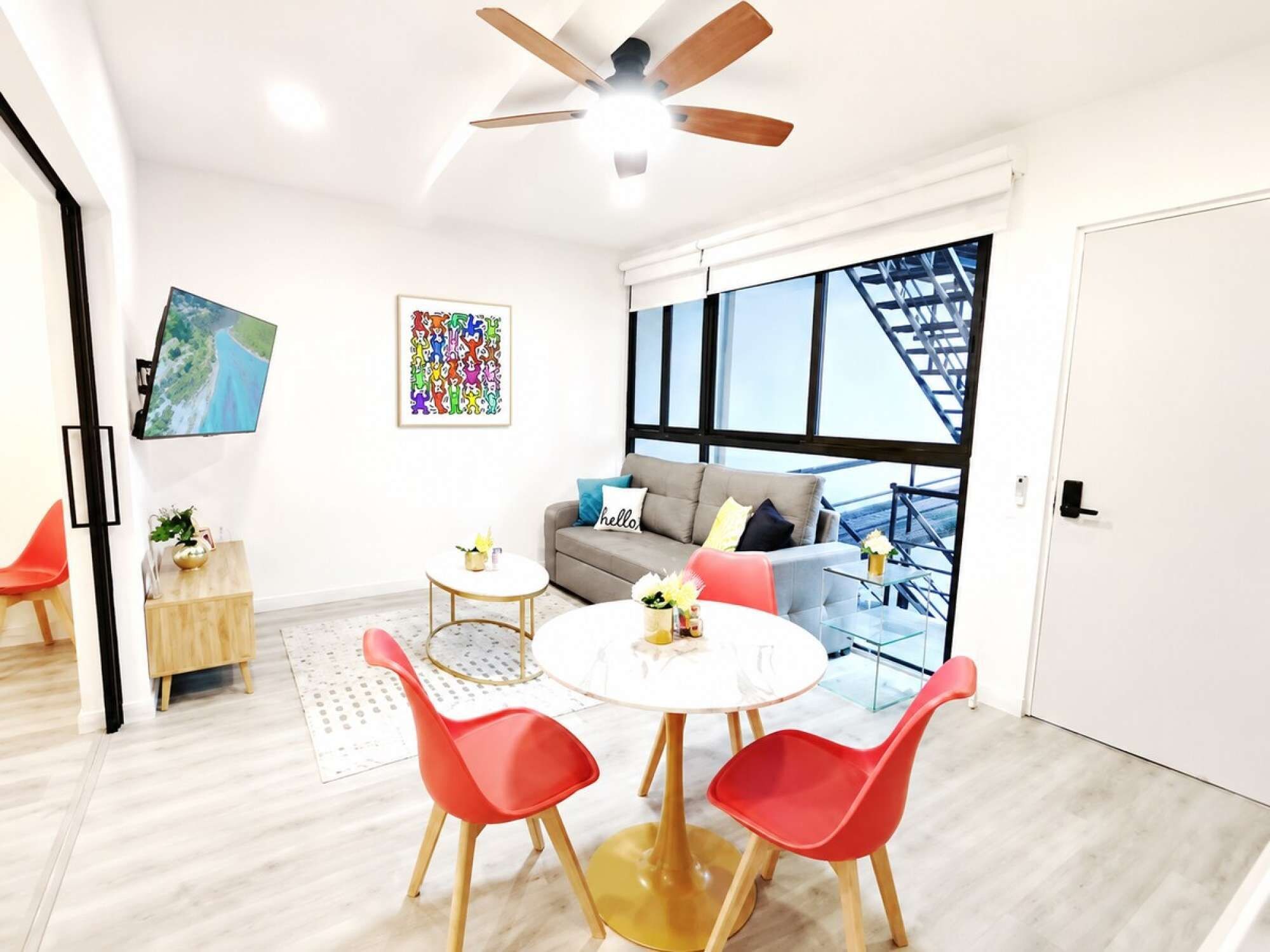 A modern living room with a sofa, a dining table with chairs, a ceiling fan, and a large window with a view of a bridge.