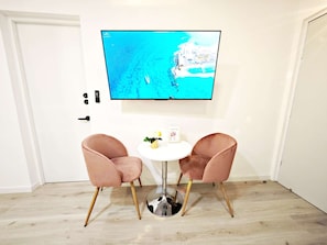 A room with a TV mounted on the wall displaying a coastal scene, two pink chairs around a small white table, and a door with a handle. - Luz María 7 y 8 · 60 m² near museums and Chapultepec · 2 baths (Ciudad de México)