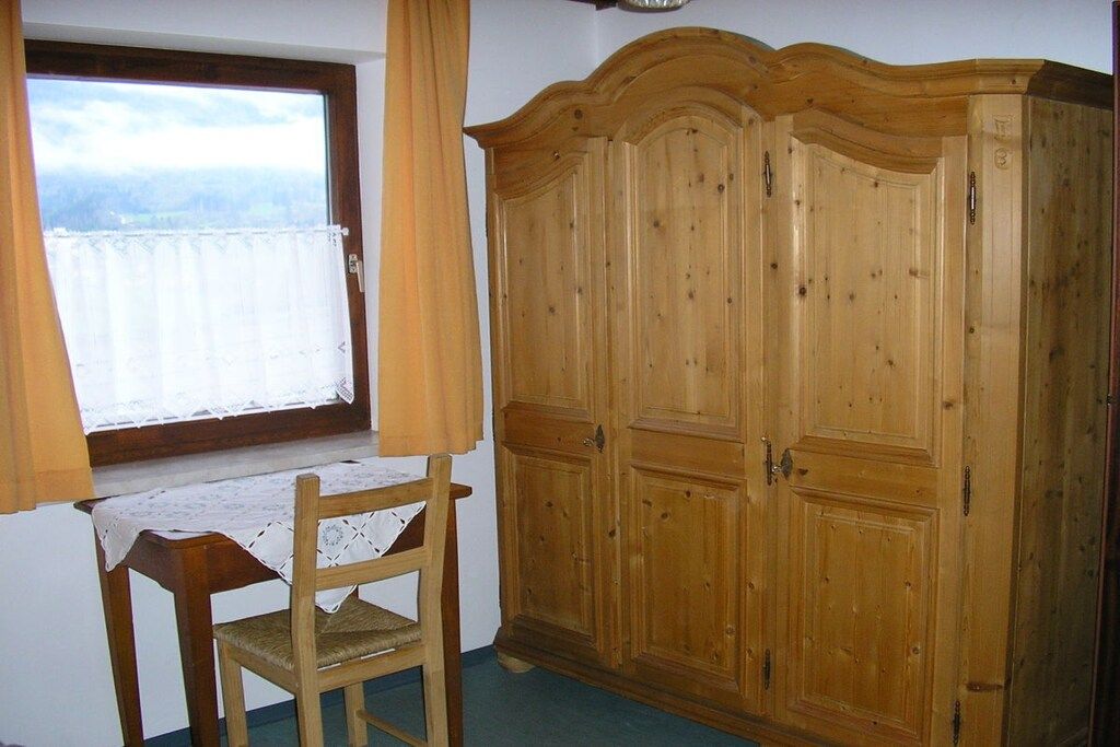 A room with a wooden wardrobe, a table with a lace tablecloth, and a chair.