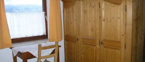 A room with a wooden wardrobe, a table with a lace tablecloth, and a chair.