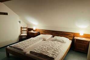 Ein Zimmer mit zwei Betten, einem Holzkopfende, Nachttischen mit Lampen, einem Sessel und einem kleinen Fenster.