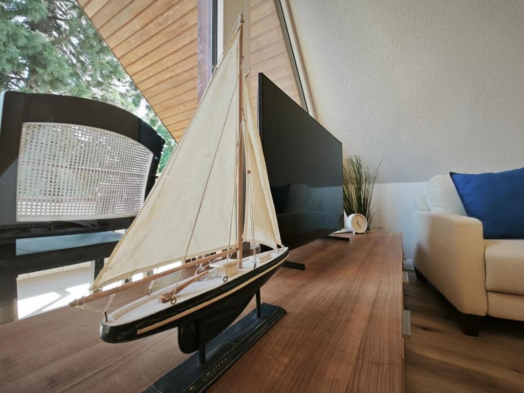 A model sailboat on a wooden table in a room with a sofa and a potted plant.