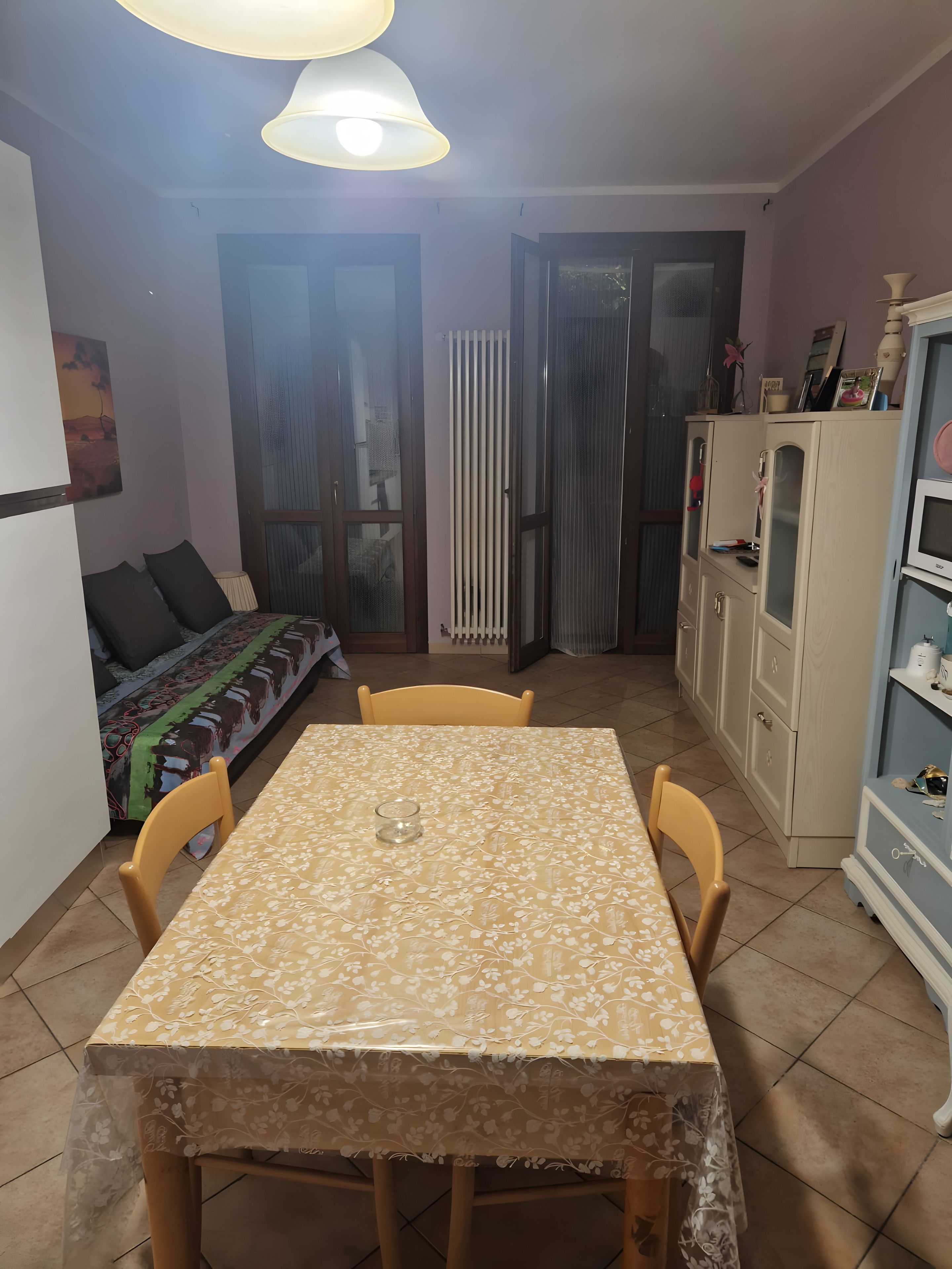 Een zithoek met een tafel bedekt met een bloemenkleed, twee stoelen, een kast met keukenapparatuur, en een bank met een gestreept kleed.